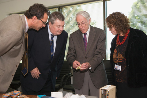 Two men and one woman leaning in to look at a small bone being held by Graeme Clark.