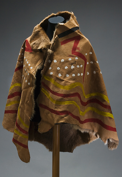 Front view of the booka, with fur on the inside, showing the painted designs using the colours red, yellow, white and black.