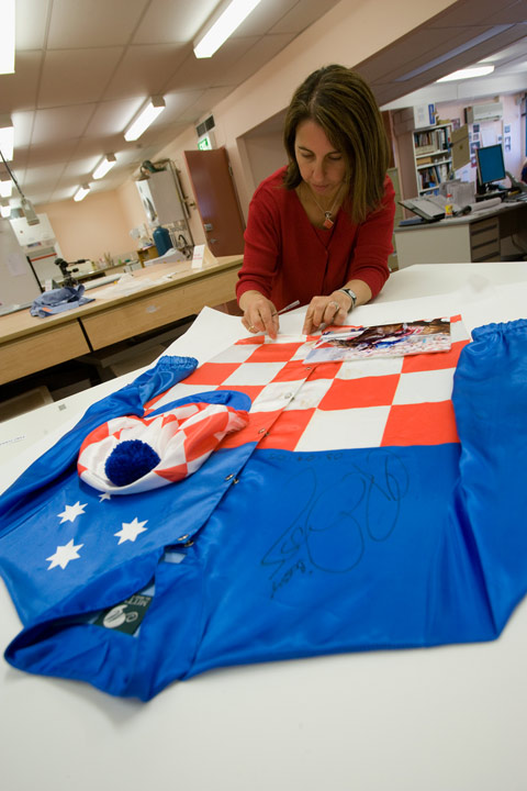 Conservator Carmela Mollica working on Makybe Diva jockey silks worn by Glen Boss. They were commercially framed using staples and double-sided tape to attach them to the backing board. This provided a challenge to conservators.