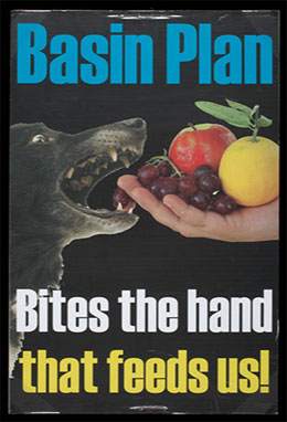 Colour photograph of a poster on a black background, with a central image of a dog biting an extended hand holding fruit. Printed text reads: 'Basin Plan. Bites the hand that feeds us!'