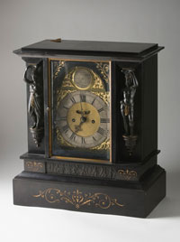 A mantelpiece clock, showing the face and one of the sides. The clock is made from dark material and has carved decorations.