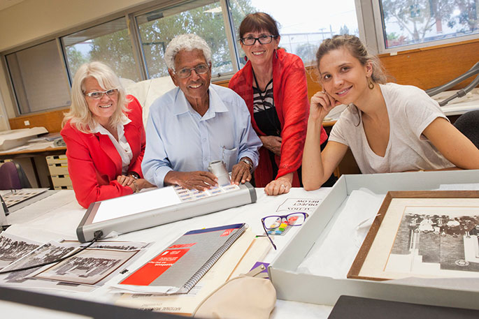 A man and three women standing at a bench, with photos and a lightbox on the benchtop.