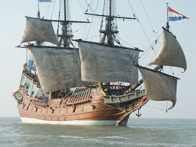 Timber sailing vessel at sea with lower sails catching the wind. The Dutch flag sails from the bowsprit.