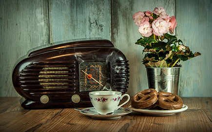 On old radio, a bucket of flowers, a cup and saucer, and a plate of biscuits.