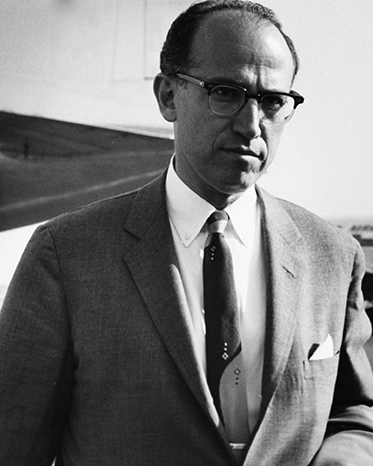portrait of a serious-looking man of about 40 in a suit, with a receding hairline, wearing glasses