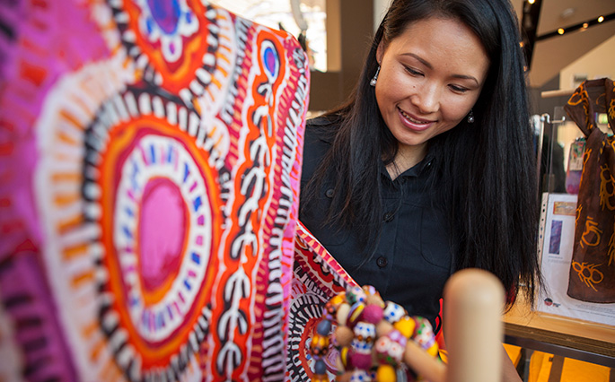 A woman looking at a scarf featuring Indigenous artwork.afts.