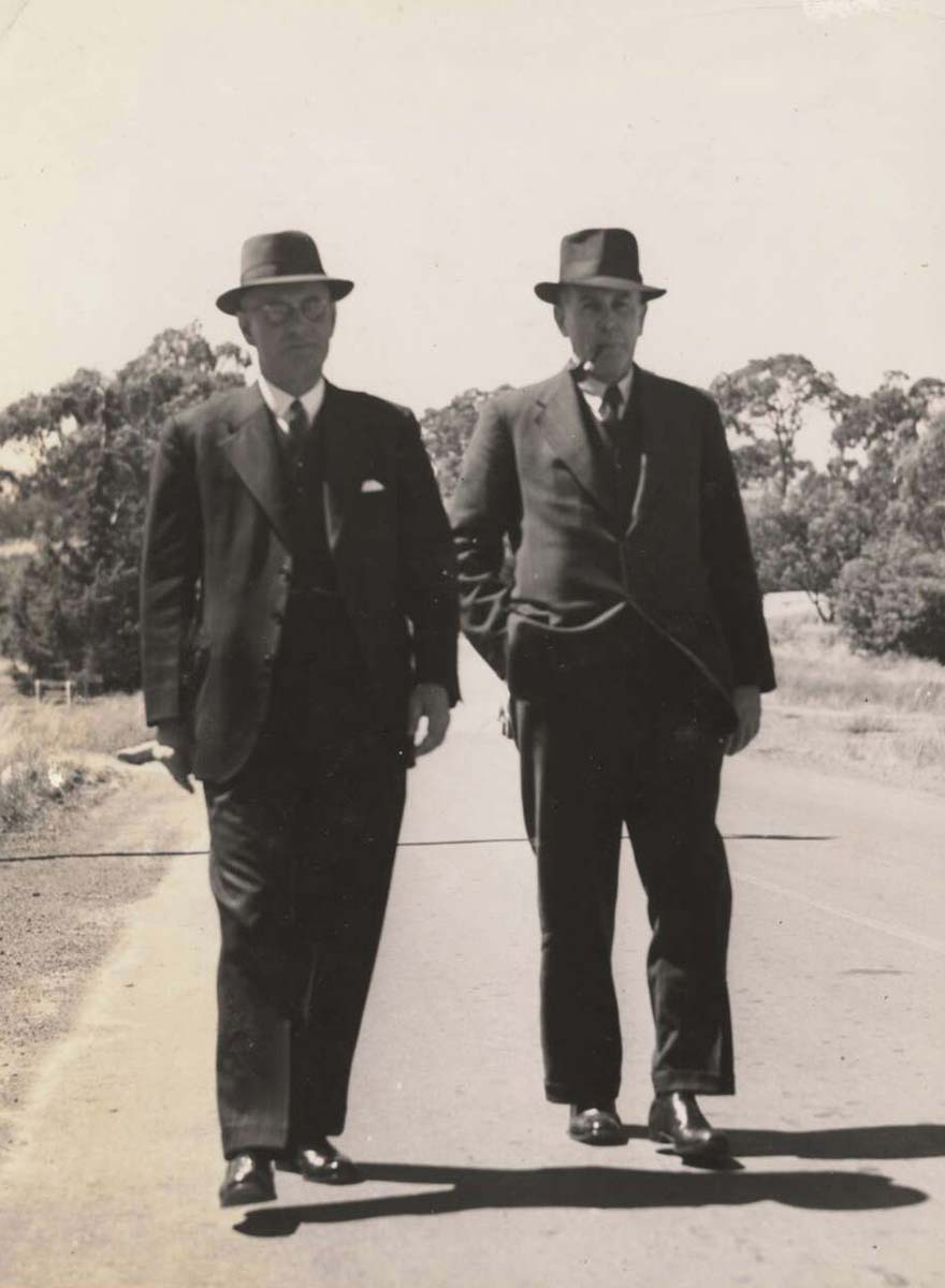 two men in suits and hats walk side by side outside.