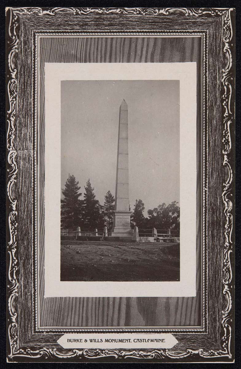 An unused postcard featuring a slightly pressed black and white photograph of a stone or concrete obelisk with a fence around it. The text reads 'BURKE AND WILLS MONUMENT, CASTLEMAINE'. - click to view larger image