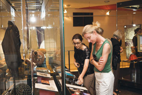 Two women look at a display panel at the front of a case containing Rolf Harris' leather jacket and wobble board.