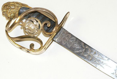 The hand grip of an 1803 military sword is of wood covered in fishskin bound with wire, and it is capped by a lion's head pommel. It is guarded by a squarish gilded brass half basket hilt, composed of a cross guard linked to the pommel by a knuckle bow and two curved bars.