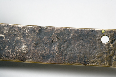 Close up image of a section of the back of the Leichhardt nameplate detailing the greyish-brown uneven surface and the fastening hole at the top in the centre.