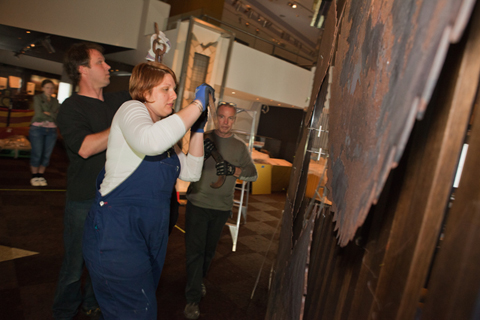 A colour photograph of three setting up a display on a wall.