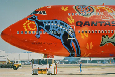 Side view of the front section of a large 'QANTAS' aircraft painted with a red background and multicoloured Aboriginal designs, including a large kangaroo.