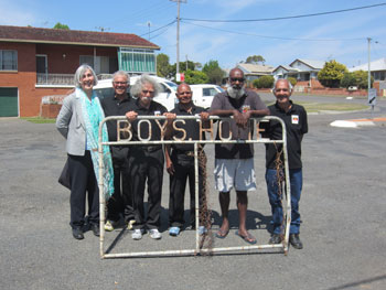 jay-arthur-2.jpg A group of people stand behind an old metal gate. The gate contains the writing "Boys Home".