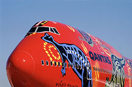 Front of a large aeroplane, painted in Aboriginal designs on a red backdrop.