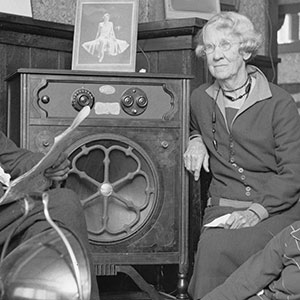 An elderly couple and two young women or girls sit around a radio the size of a bar fridge