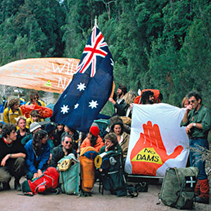 Young people squatting or standing on a dirt road holding the Australian flag and various banners.