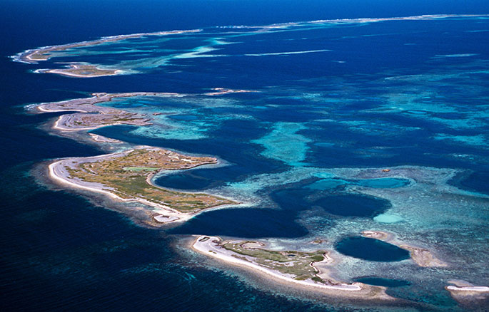 Aerial shot of five islets surrounded by reefs and deeper sea