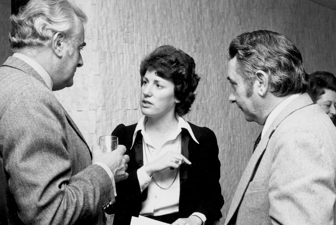Interior photo. Woman in her thirties is speaking while Whitlam and Oswin listen