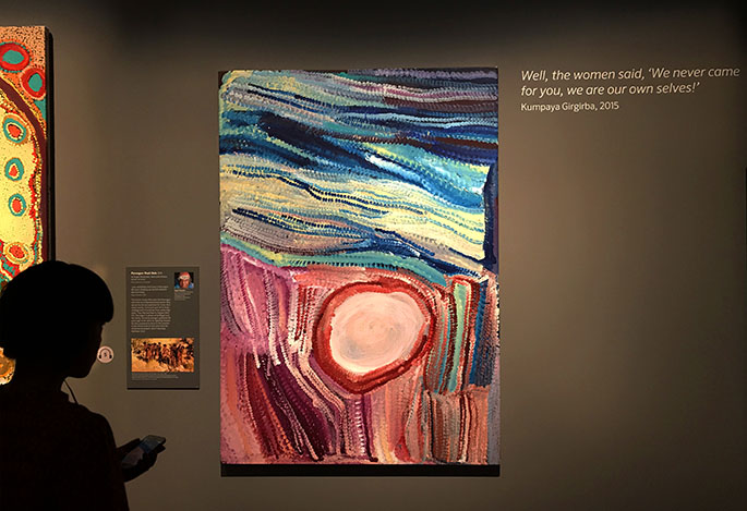 Female with headphones, standing in front of a painting from the Songlines exhibition