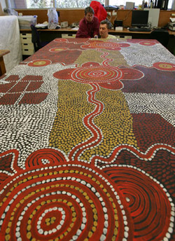 Two conservators inspect far end of large Yumari 1976 dot painting by Uta Uta Tjangala.