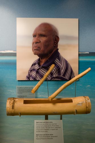 A display that showcases a drum and drum sticks from the Mer region together with an image of one of the three Torres Strait Islander men who fought the Mabo case, Father Dave Passi (2000).