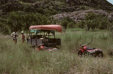 Two three-wheel motor bike, canoe upside down on a rack and two people in the background.