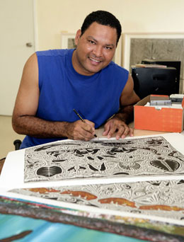 A man holding a black pen sits at a bench, working on a drawing.