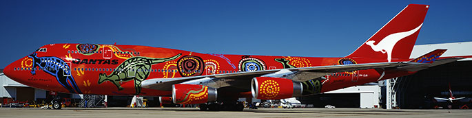 Side view of a large plane with Aboriginal designs painted on a red background.