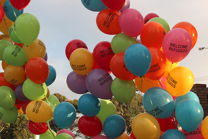 Multicoloured balloons with 'Welcome Refugees' on them flying in the air