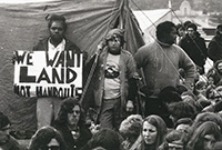 Aboriginal Land Rights Act Aboriginal man standing in front of tent holding up sign saying ‘We want land not handouts’. He is surrounded by a dozen or so other protesters.