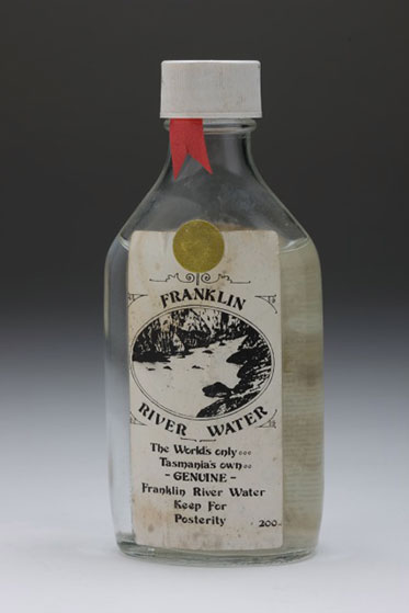 studio shot of bottle of water with a dirty label reading Franklin River water. The world’s only. Tasmania’s own. Genuine Franklin River Water. Keep for posterity. 200 ml