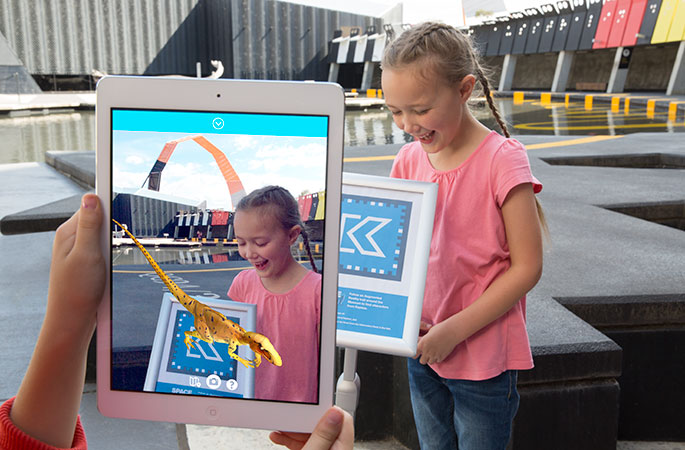 A young girl uses an electronic tablet to play a game which reveals a virtual dinosaur