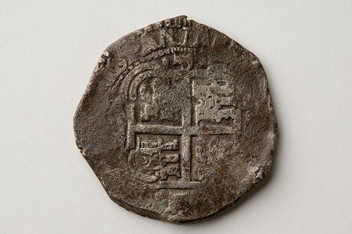 Studio photo of worn and battered silver coin whose imprint is barely discernible.