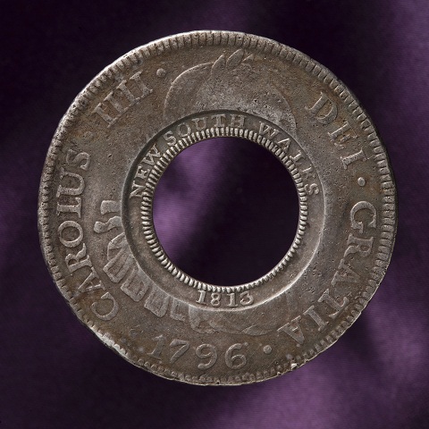 Circular coin with a hole at the centre. 'NEW SOUTH WALES 1813' is stamped around the centre ring. 'CAROLUS IIII DEI GRATIA 1796' is stamped around the outer rim.