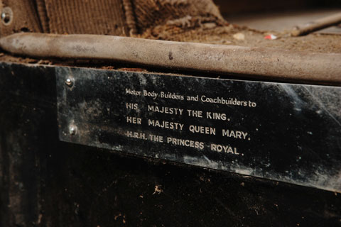 A metal plate attached to the bodywork of an historic vehicle. Text on the plate says 'Motor Body Builders and Coachbuilders to His Majesty The King, Her Majesty Queen Mary, H.R.H. The Princess Royal.'