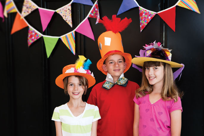 Three children dressed in colourfully decorated top hats.