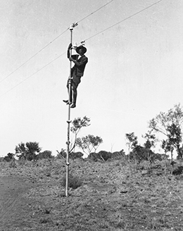 A black and white photo taken in the 1920s of a man who has climbed up to the top of a pole