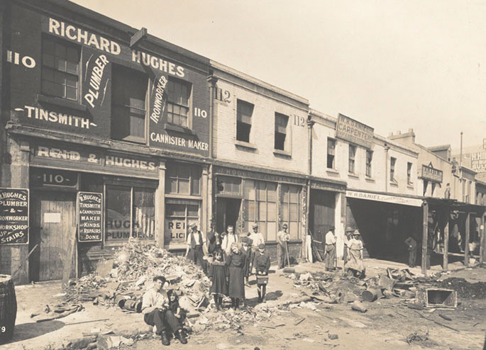 A dozen or so people pose in front of shop fronts amid rubbish that has been removed from the interiors of buildings