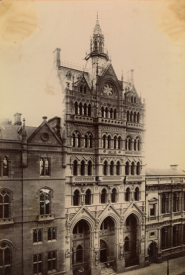 An ornate gothic building seven or eight storeys high with lower buildings on either side