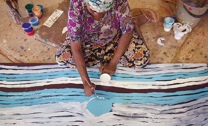 Songlines catalogue spread showing an aerial image of a woman painting a large canvas