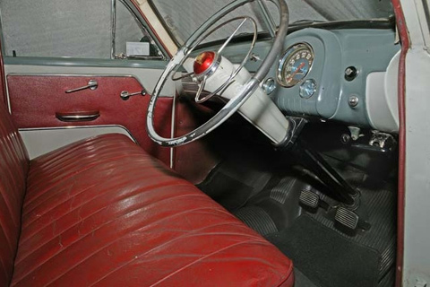 Interior view of a car showing a blue-grey body with red bench seat and right hand side drive.