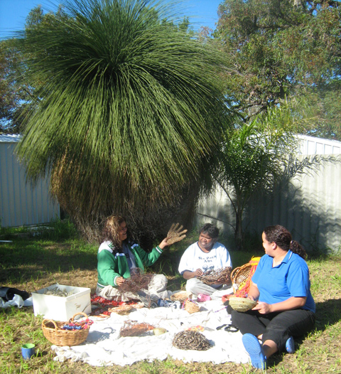 Three women weaving under a tree