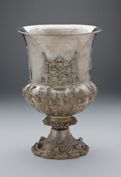 An ornate sterling silver cup with a central engraving and coat of arms.