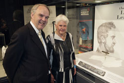 Colour photograph showing a man and woman standing beside a display case, with a small metal plate partially visible at the right.