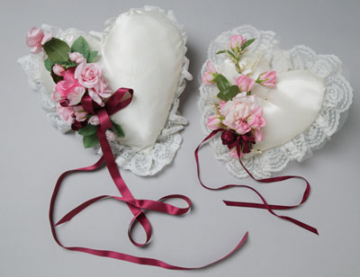 Two love-heart shaped cushions, similar in appearance, decorated with maroon ribbons and pink flowers.