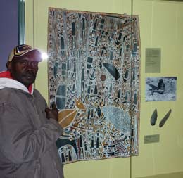 Daniel Wilfred standing besdie a bark painting of Ngilipidji by Djardi Ashley