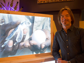 jono-lineen-2.jpg A man stands to the side of a video display depicting a man holding a sea turtle and egg.