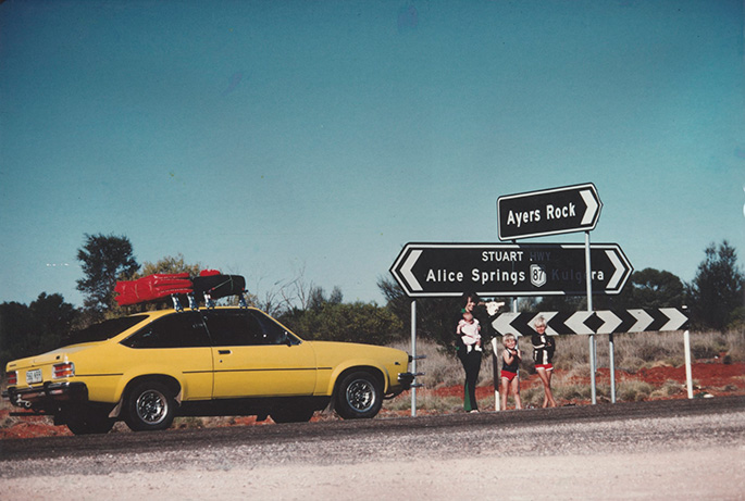 Lindy Chamberlain holding Azaria Chamberlain, with Aidan and Reagan Chamberlain, standing on Stuart Highway with sign to 'Ayers Rock', alongside their Torana, 16 August, 1980.