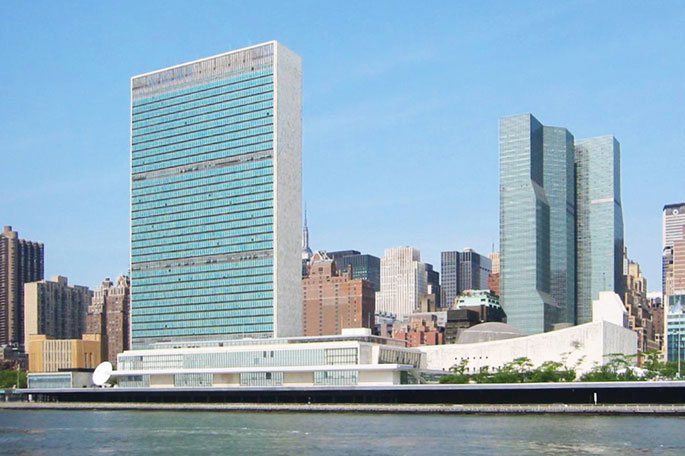 Large glass and concrete building on bank of river, with other buildings on either side